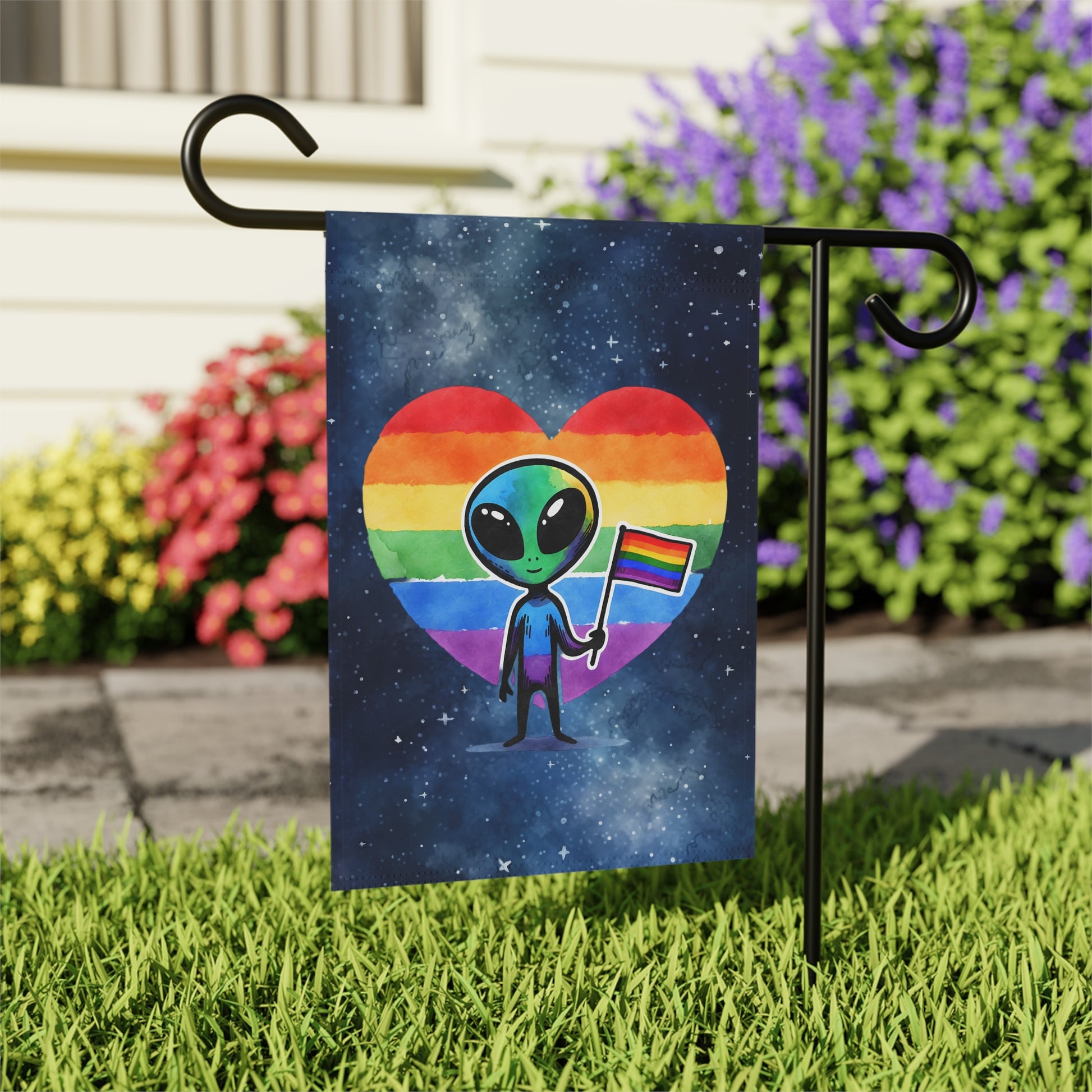 Garden flag with an alien holding a rainbow flag inside a heart on grass with flowers in the background