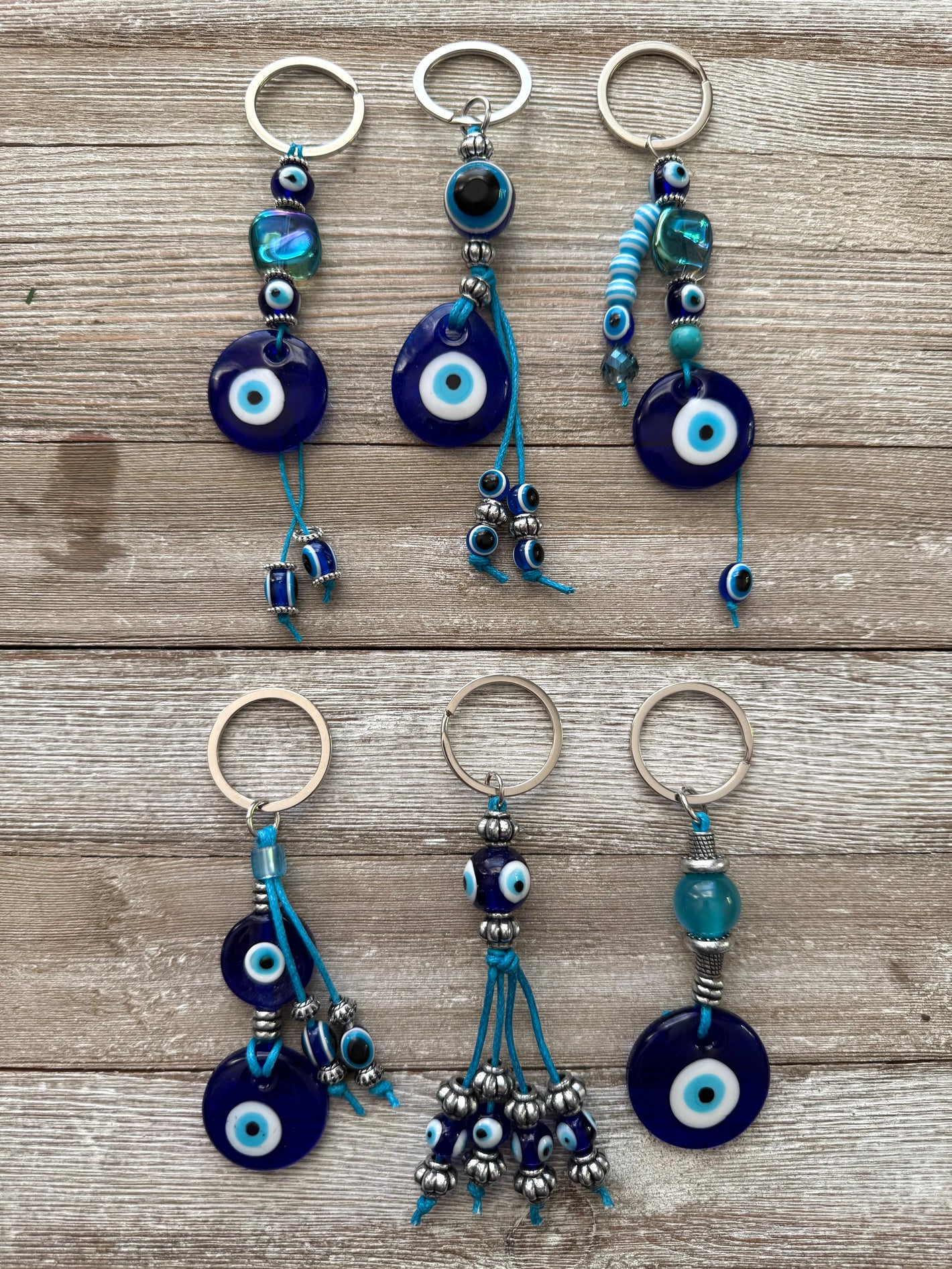 A collection of handmade beaded keychains with metallic and glass beads, featuring a navy blue and silver-tone hardware, displayed on a wooden surface.
