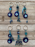 A collection of handmade beaded keychains with metallic and glass beads, featuring a navy blue and silver-tone hardware, displayed on a wooden surface.