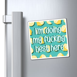 A square refrigerator magnet with a bold graphic design, shown attached to a brushed stainless steel refrigerator door next to the handle. The magnet features a turquoise background patterned with yellow lemon slices and the text 'I'm doing my fucking best here' in white stylized lettering.