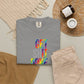 Gray t-shirt with colorful text on a neutral surface with pants and decor items.