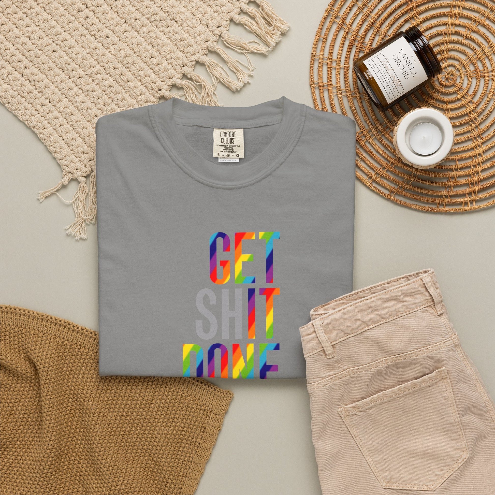 Gray t-shirt with colorful text on a neutral surface with pants and decor items.