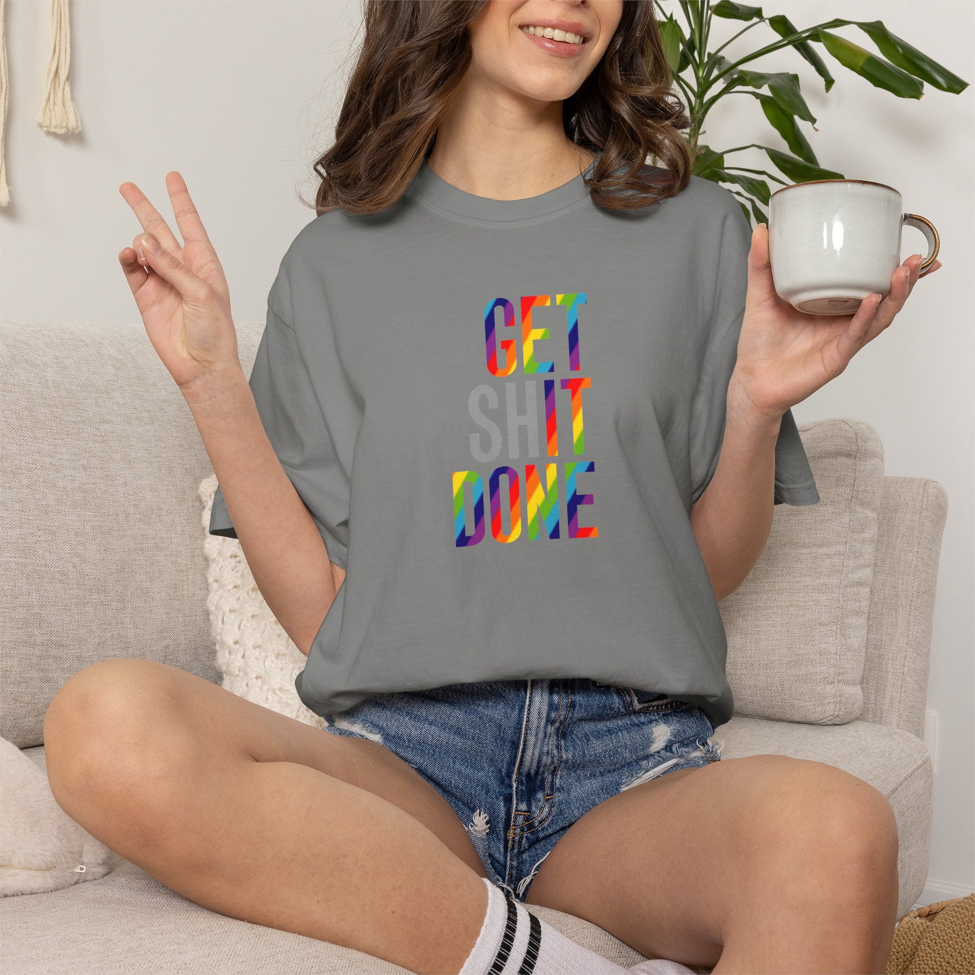Person wearing a gray t-shirt with colorful text, sitting on a couch holding a mug.