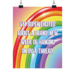 A colorful poster featuring a rainbow graphic with the text 'I'M SUPER EXCITED ABOUT A BRAND-NEW WEEK OF HANGING ON BY A THREAD.' in large white letters with a purple outline, shown hanging from two black clips against a white background.