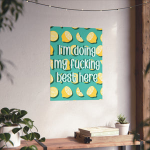 A vertical canvas wall art print featuring a teal background with yellow lemon illustrations and the text 'I'm doing my fucking best here' in white with a black outline. The canvas is displayed hanging on a textured off-white wall in a styled room setting with a wooden console table, potted plants, and string lights.
